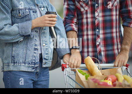 Mid-section portrait of contemporary young couple pushing shopping cart with groceries in parking lot, copy space Stock Photo