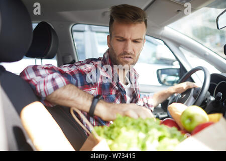 Portrait of young man sitting in car with groceries, copy space Stock Photo