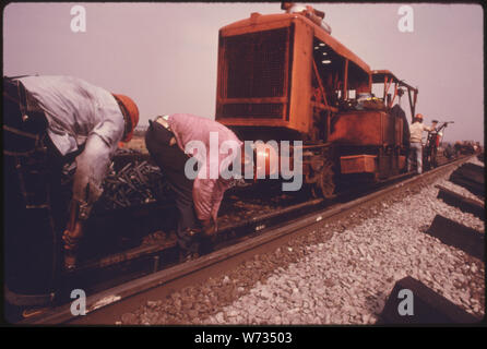 SOUTHERN RAILWAY RIGHT-OF-WAY WORK CREW WITH MACHINERY USED TO REPLACE OLD TRACK WITH NEW QUARTER MILE LONG SECTIONS OF RAILS. ON A GOOD DAY, WHEN THE CREW DOESN'T HAVE TO STOP WORK TOO MANY TIMES TO LET TRAINS PASS ON PARALLEL TRACKS, THEY CAN LAY SLIGHTLY LESS THAN TWO MILES OF WELDED TRACKS PER DAY. IN 1974 SOUTHERN HAD AN AVERAGE OF FOUR CREWS NUMBERING 50 TO 55 MEN EACH WORKING ON THE SYSTEM'S 10,531 MILES OF TRACK. IN THAT YEAR, SOUTHERN SPENT 18.6 PERCENT OF ITS REVENUE ON MAINTENANCE Stock Photo