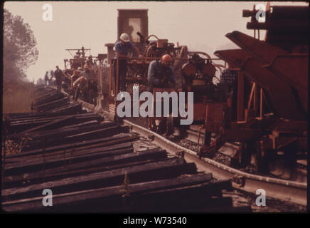 SOUTHERN RAILWAY RIGHT-OF-WAY WORK CREW, WITH MACHINERY USED TO EXCHANGE OLD TRACK FOR NEW QUARTER MILE LONG SECTIONS OF RAIL. NOTICE THE NEW STACKS OF RAILROAD TIES IN THE LEFT FOREGROUND ON A GOOD DAY, WHEN THE CREW DOESN'T HAVE TO STOP WORK TOO MANY TIMES TO LET TRAINS PASS ON PARALLEL TRACKS, THEY CAN LAY SLIGHTLY LESS THAN TWO MILES OF WELDED TRACKS PER DAY. IN 1974 SOUTHERN SPENT 18.6 PERCENT OF ITS REVENUE IN TRACK MAINTENANCE Stock Photo