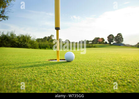 Close up low angle view of a golf ball on the green near the hole on a sunny afternoon