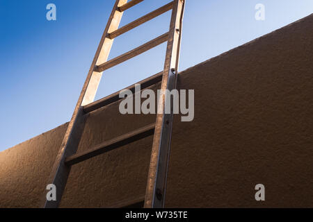 Low angle view of metal ladder leaning against concrete wall, conceptual themes of overcoming obstacles, challenges and new opportunities. Copy space. Stock Photo