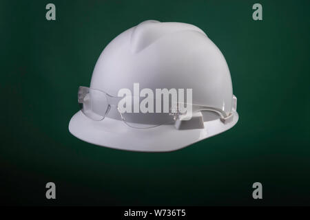 White generic protective construction helmet with a plastic transparent safety glasses on the cap against a green studio background Stock Photo