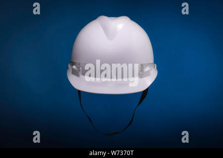 White generic protective construction helmet with strap and plastic transparent safety glasses on the cap against a blue studio background Stock Photo