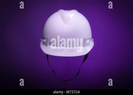 White generic protective construction helmet with strap and plastic transparent safety glasses on the cap against a purple studio background Stock Photo