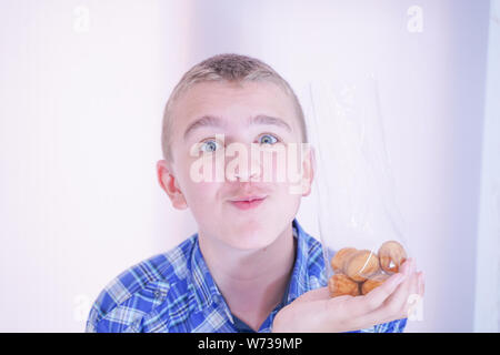 cute hungry teenager boy with fresh small bake sweets on white room background alone Stock Photo