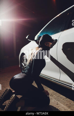 Masked robber woman car The thief is levering the lock at the door car robbery. Stock Photo
