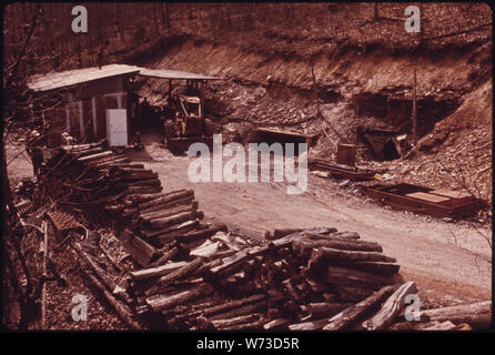 VIEW OF THE MINE OF GEORGE WILSON NEAR WILDER AND COOKEVILLE, TENNESSEE, WHICH WAS CLOSED DOWN BECAUSE IT LACKED A NON-ARCING DRILL. THE WOOD IN THE FOREGROUND IS FOR TUNNEL ROOF BRACES, AND THE LOADER IN THE BACK-GROUND FOR COAL AT THE TIPPLE JUST TO THE RIGHT OF THE LOADER IS THE MAIN SHAFT OPENING, AND TO THE RIGHT OF THE SHAFT IS THE ESCAPE TUNNEL AND AIRWAY. NOTE THE TWO SMALL SHUTTLE CARS WHICH ARE RUSTED AND WITHOUT WHEELS, TYPICAL OF THE WASTE AT SMALL MINES Stock Photo