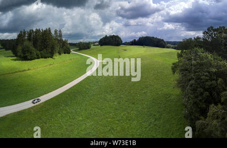 Aerial of car driving along countryside road through green fields in summer Stock Photo