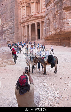 A group of tourists & 2 donkeys pose for a photo in front of the Treasury, an elaborate temple in the ancient city of Petra in Jordan. Stock Photo