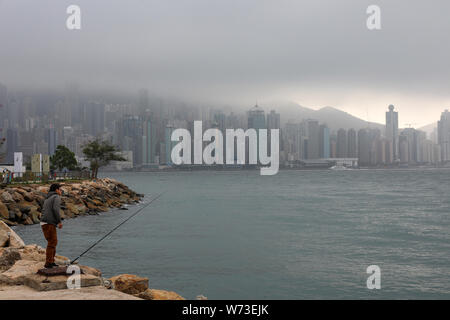 Man with a fishing rod in Yau Ma Tei, Hong Kong Island skyscrapers in the backgroung, on a foggy day Stock Photo