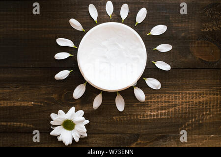 Skin care. The concept of solar skin care. White mask for the body and face on a wooden table of the sun. Petals in the shape of the sun. Top view Stock Photo