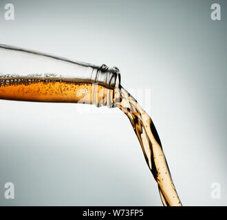 Hard cider poured from clear bottle. Stop action closeup on grey background Stock Photo
