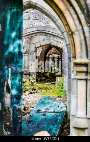 View through a derelict church, located in the grounds of Flaybrick Memorial Gardens.  The corrider runs the width of the church, and has no roof and a number of bricks at the end from a collapsed wall.  At the front are the remains of the arched double doors, in a vibrant turquoise colour.