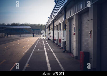 Traffic light at the exit of the deserted original pit lane at Silverstone race track.  Garages on the right of the frame. Stock Photo