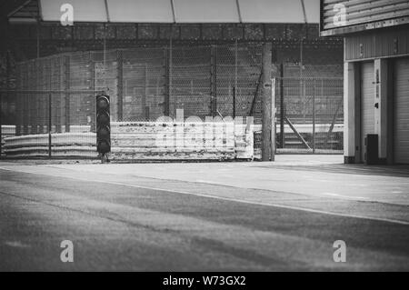 Black & White images of the traffic light at the exit of the deserted original pit lane at Silverstone race track.  Garages on the right of the frame. Stock Photo