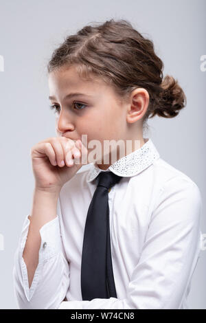 Thoughtful little schoolgirl with hand to her mouth staring ahead with a contemplative serious expression in a close up portrait Stock Photo