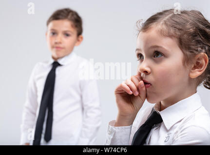 Thoughtful little girl with hand to mouth looking up with a pensive expression as she seeks the solution to a problem or formulates a bright idea with Stock Photo