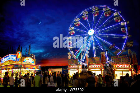 A ferris wheel under a crescent moon on a summer evening brings to mind childhood memories. A good old fashioned carnival is an American tradition. Stock Photo