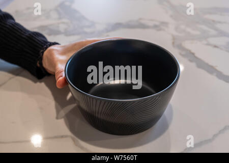 Female hand holding empty black bowl on white marble kitchen top Stock Photo
