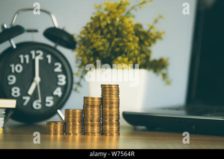 Coin stack and financial graph paper sheet with notebook calculator and alarm clock on working table, business finance concept idea. Stock Photo