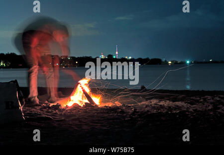 Unrecognizable person with blurred motion making beach camp fire with CN Tower along Toronto skyline by Lake Ontario under stars in the sky. Blurred m Stock Photo