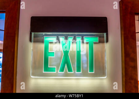 Building interior with a neon green light Exit sign pounted on the white wall Stock Photo