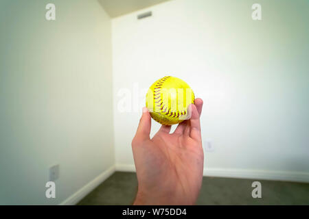 Close up of a hand holding a baseball with white wall in the background Stock Photo