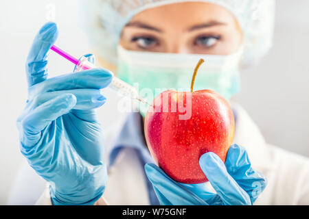 A biologist woman genetically modifies an apple for longer life. Female researcher or scientist using laboratory equipment for syringe and needle in s Stock Photo