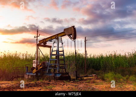 Oil rig pump against a colorful sunset sky Stock Photo