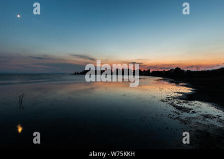 Moon above a lake with its reflection on the Trasimeno lake surface at dusk Stock Photo