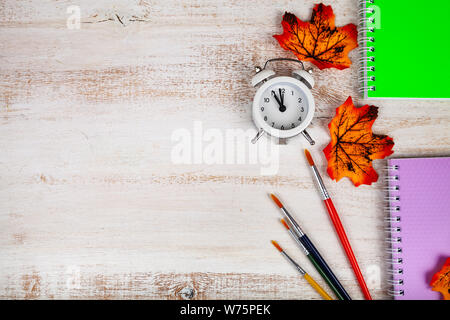 Back to school. Alarm clock, notebooks, brushes and autumn leaves on a wooden table. Stock Photo