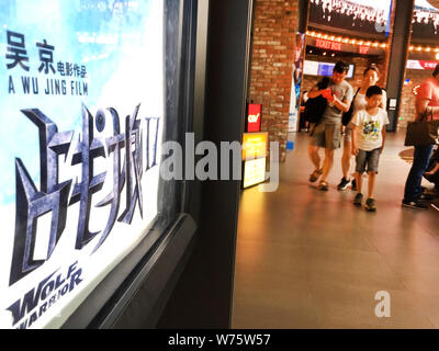 --FILE--Chinese film goers walk past a poster of the Chinese action movie "Wolf Warriors 2" displayed at a cinema in Shanghai, China, 19 August 2017. Stock Photo