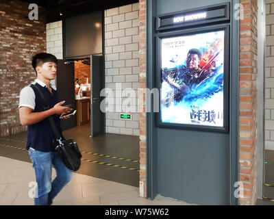 --FILE--A Chinese film goer walks past a poster of the Chinese action movie "Wolf Warriors 2" displayed at a cinema in Shanghai, China, 19 August 2017 Stock Photo