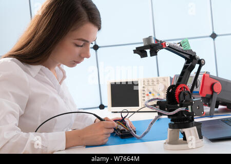 A young woman writes an algorithm for the robot arm. Science Research Laboratory for Robotic Arm Model. Computer Laboratory Stock Photo