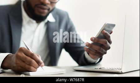 African American businessman looking at smartphone taking notes in office Stock Photo