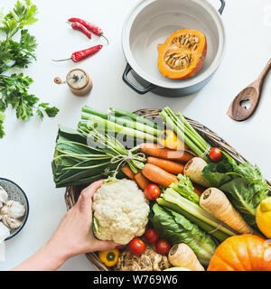 Healthy seasonal food. Autumn cooking with pumpkin. Female hand holding ingredients on white desk with various colorful organic farm vegetables , pot Stock Photo