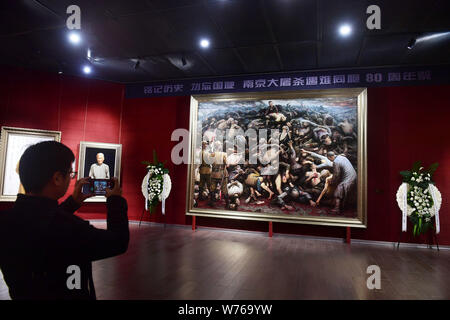 A visitor takes photos of the oil painting 'Nanjing Massacre' by US-based Chinese artist Li Zijian on China's fourth National Memorial Day for Nanjing Stock Photo
