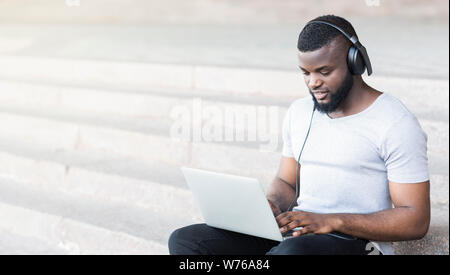 Concentrated african guy in headphones typing on his laptop Stock Photo