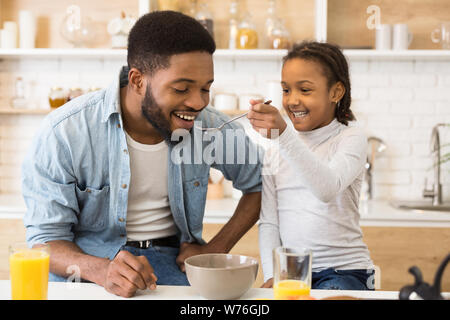 Adorable afro girl feeding her dad cereals Stock Photo