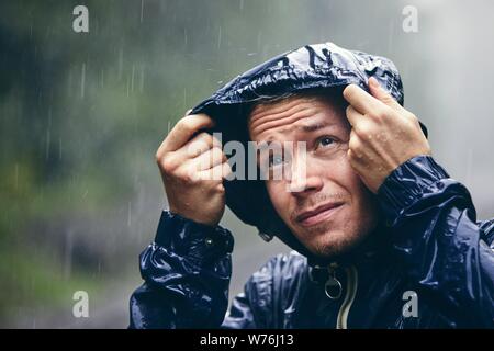 Trip in bad weather. Portrait of young man in drenched jacket in heavy rain. Stock Photo