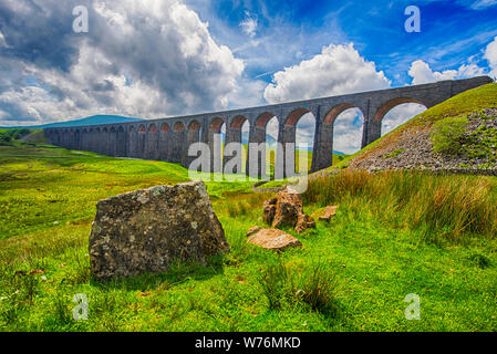 View of a large old Victorian railway viaduct across valley in rural countryside scenery panorama with stone wall Stock Photo