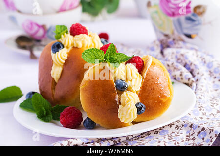 Rum baba decorated with whipped cream and fresh raspberry, blueberry. Savarin with rum, cream and berries. Italian cuisine Stock Photo