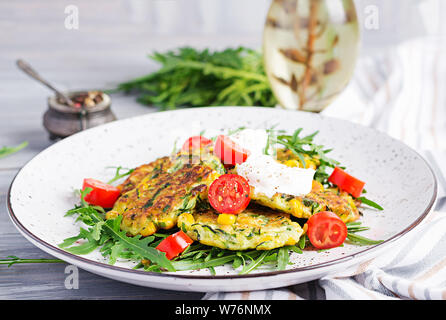 Zucchini pancakes with corn and sour cream served arugula, tomatoes salad. Stock Photo