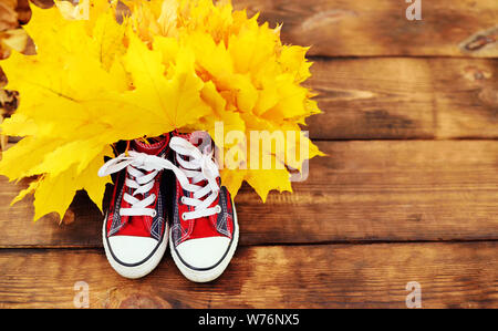 red bright sneakers with yellow autumn foliage on a wooden background. Stock Photo