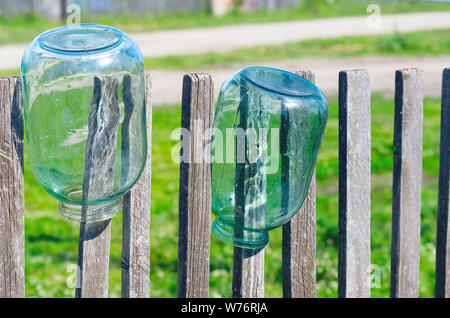 Washed Three Liter Glass Jars Left to Dry Upside Down on Weathered Timber Picket Fence on a Sunny Summer Day. Stock Photo