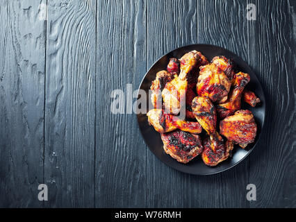 Spicy Grilled Caribbean Jerk Chicken drumsticks and thighs on a black platter on a wooden table, view from above, flat lay, empty space Stock Photo