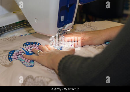 Woman dressmaker works by hands on overlock. Industrial Stock Photo