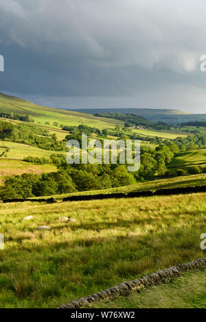 Dark cloudy sky & long-distance picturesque evening view to Wharfedale (rolling hills, green pasture, sunlit valley) - Yorkshire Dales, England, UK.