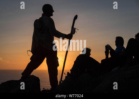 Pilgrims on the Cape Finisterre, which marks the end of the Camino de Santiago in Spain. Silhouette of a man on rocks with a walking stick, talking wi Stock Photo